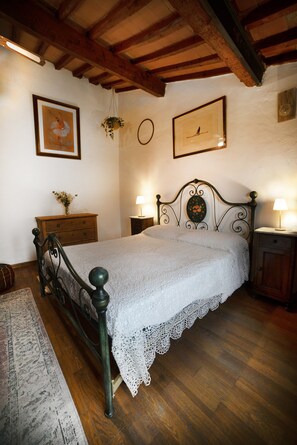 A bedroom with a wooden bed frame, a white bedspread, a wooden nightstand with a lamp, a wooden dresser, and a hanging plant. - Poetic Florence - Spacious Central Home: 3-BR, 2-Bath, Lift, View & Parking (Firenze)
