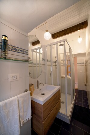 Un baño con ducha envuelta en vidrio, tocador de madera, lavabo blanco y espejo.