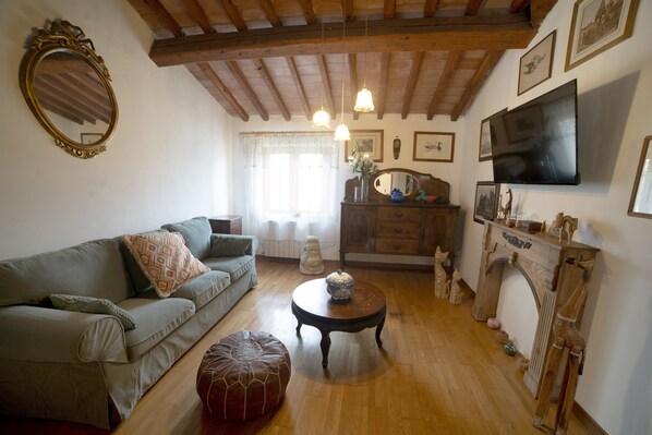 Una sala de estar con sofá, reposapiés, mesa de centro de madera, chimenea y televisor montado.