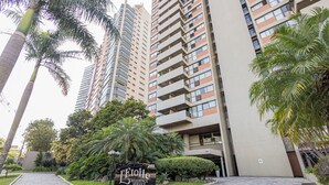 Un immeuble résidentiel moderne, avec une enseigne indiquant « L’Étoile Residence Service », et une zone d’entrée pavée agrémentée de palmiers.