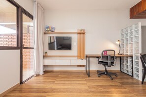 A modern office space with a wooden desk, office chair, and a TV mounted on the wall. - LTL - L'Etoile Residence by Anora Spaces (Barueri)