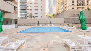 Une piscine entourée d’immeubles de grande hauteur, avec des chaises longues et des parasols.
