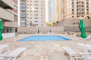 A swimming pool with lounge chairs and umbrellas, surrounded by high-rise buildings. - LTL - L'Etoile Residence by Anora Spaces (Barueri)