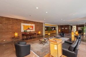 A hotel lobby with a brick wall, a reception desk, seating areas, and a large painting. - LTL - L'Etoile Residence by Anora Spaces (Barueri)
