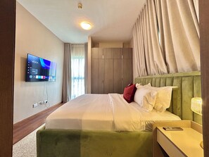 Et hotelværelse med seng, tv ophængt på væggen, et natbord med lampe og et klædeskab.