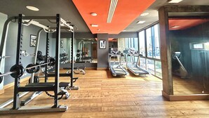 Un gimnasio con equipo de levantamiento de pesas, cintas de correr y amplios ventanales.