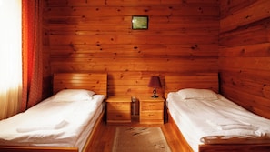 Una habitación de cabaña de madera con dos camas, una mesita de noche con lámpara y un cuadro pequeño en la pared.