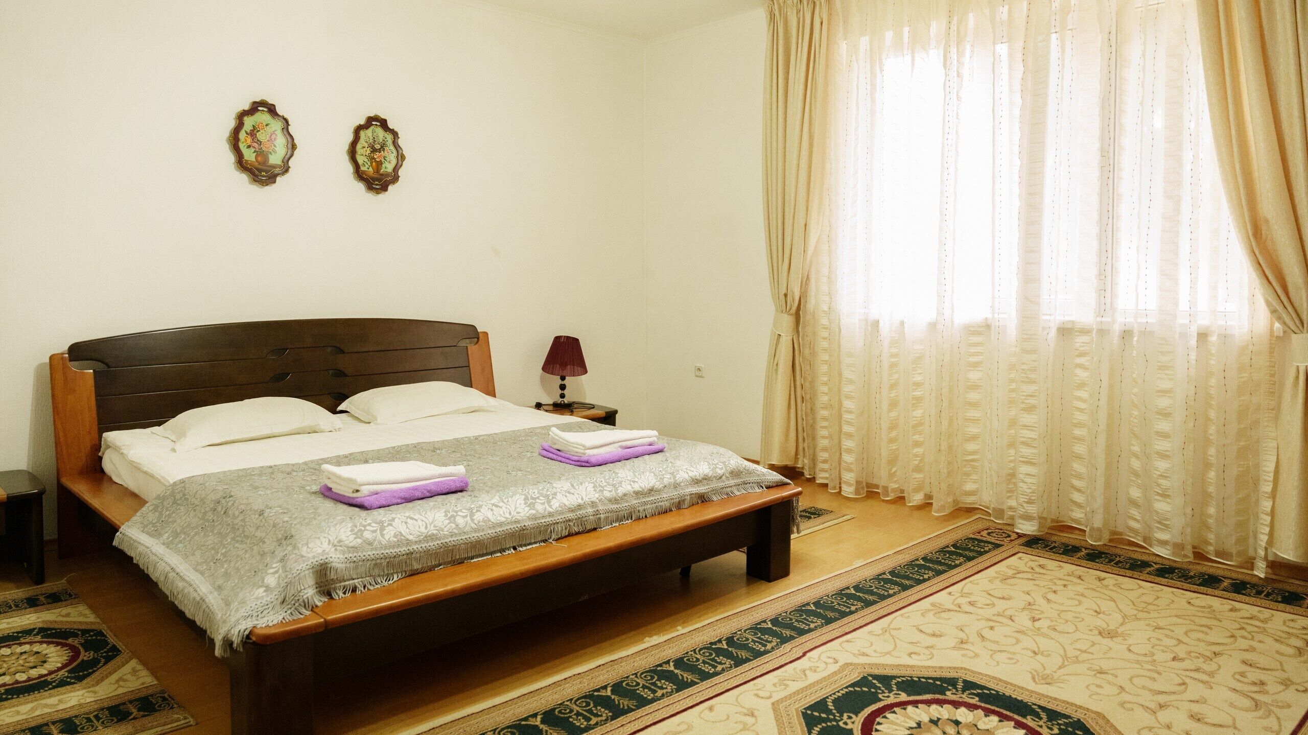 Una cama bien hecha con cabecera, una mesita de noche con lámpara y una alfombra decorativa.