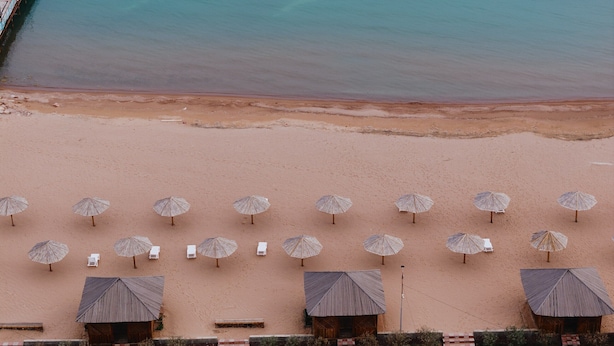 Vista aérea de una playa con filas de tumbonas y sombrillas, una estructura de madera y una vista despejada del océano.