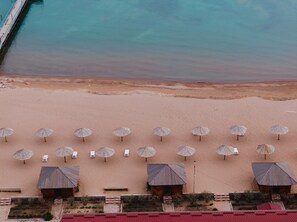 An aerial view of a beach with rows of sunbeds and umbrellas, a wooden structure, and a clear view of the ocean. - Ohotnyy Dvor Korumdu (Korumdu)