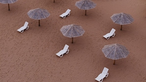 Una playa con sillas de descanso blancas y sombrillas de paja.