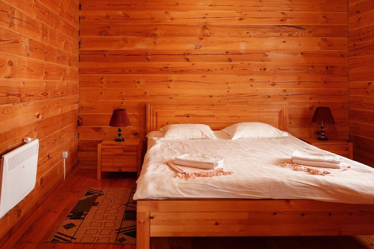 Una habitación tipo cabaña de madera con cama, dos mesitas de noche y un radiador.