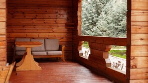 Interior de una cabaña de madera con sofá, una mesita y ventana con vistas a un paisaje nevado.