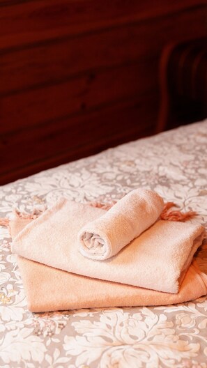 Una cama con colcha estampada con motivos florales y dos toallas dobladas.