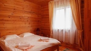 A wooden cabin room with a bed, a nightstand, and a window with sheer curtains. - Ohotnyy Dvor Korumdu (Korumdu)
