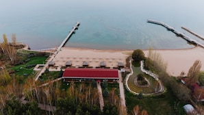 Vista aérea de un complejo turístico costero con playa, muelle y un edificio central con techo rojo.