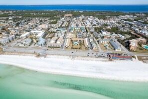 Vista aérea de un pueblo costero con playa, edificios residenciales y un amplio estacionamiento.