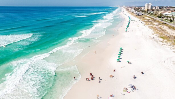 Una spiaggia con un lungo tratto di sabbia bianca, alcune persone e una fila di ombrelloni verdi.