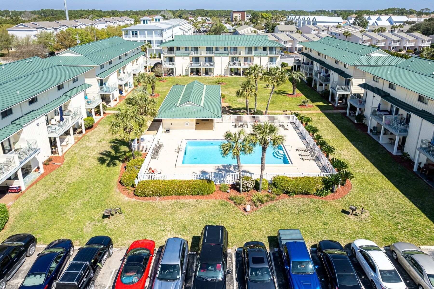 Hotel com vários andares, piscina central, estacionamento e áreas verdes ao redor.