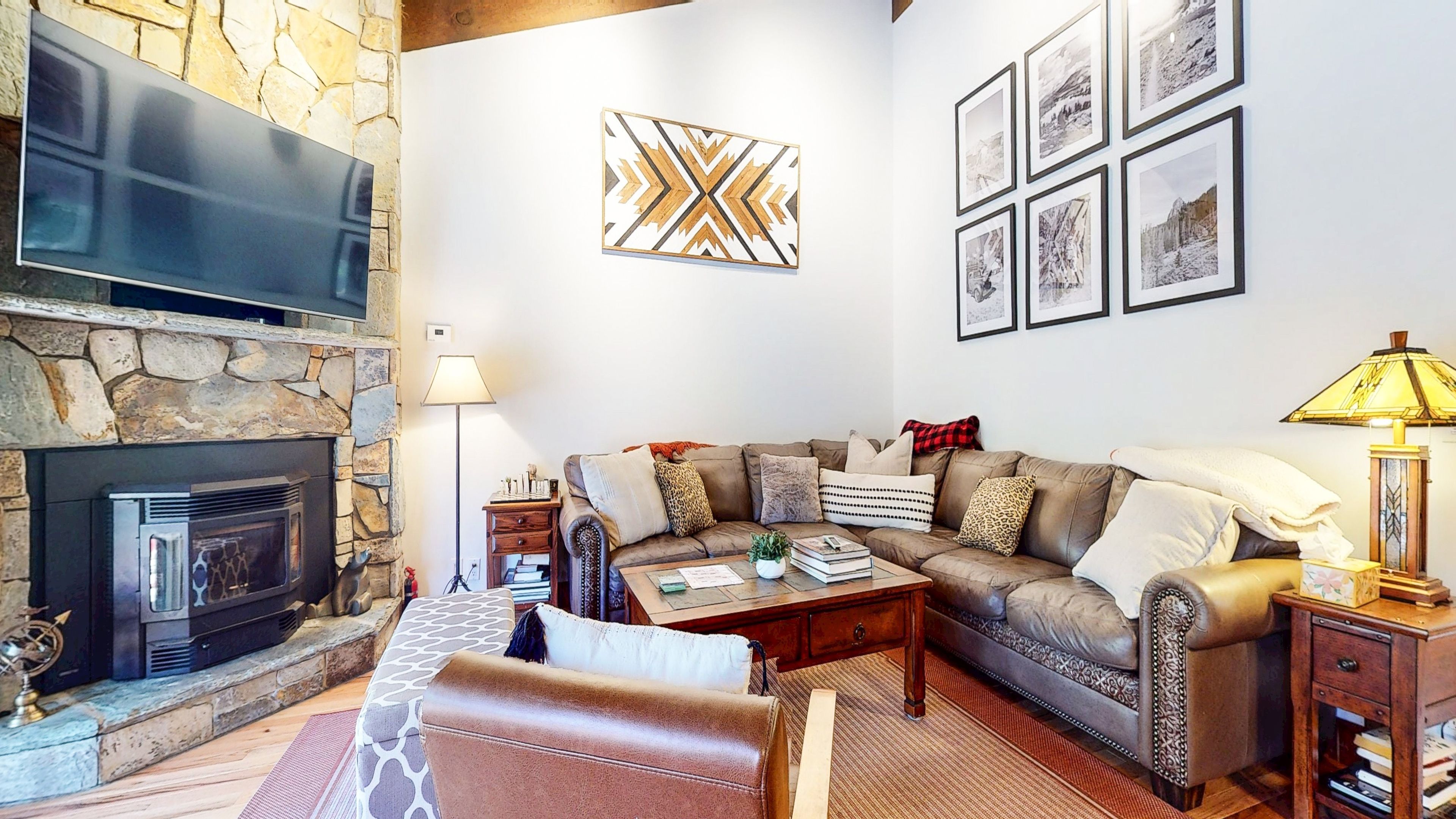 A cozy living room with a stone fireplace, a leather sofa, a coffee table, and a flat-screen TV mounted above the fireplace.