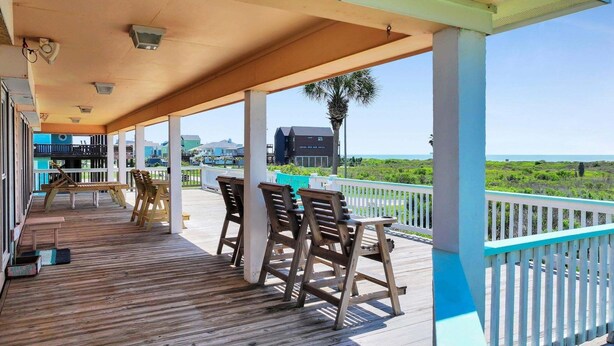 Una terraza de madera con mobiliario exterior, piscina y vista a la playa y al océano.