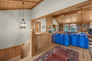 A spacious living area with a wooden staircase, a large rug, and a bookshelf filled with books. - Beachcomber's Retreat *Beach*Golf*Pets (Gearhart)