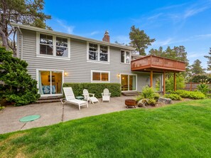 Ein zweistöckiges Haus mit einer überdachten Terrasse, einer Haustür und einem kleinen Garten mit Rasen und einigen Pflanzen.