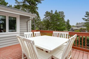 A deck with a white table and chairs, surrounded by a wooden railing, with trees and a house in the background. - Beachcomber's Retreat *Beach*Golf*Pets (Gearhart)