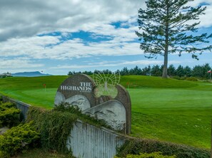 En skylt vid en golfbana med texten ”The Highlands at Gearhart”, omgiven av grönska och en klar himmel.