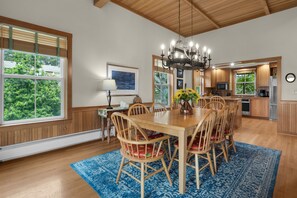 A dining area with a wooden table and chairs, a chandelier, and a view of the outdoors through large windows. - Beachcomber's Retreat *Beach*Golf*Pets (Gearhart)