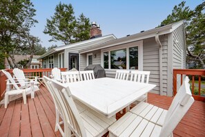 A deck with a white table and chairs, a covered grill, and a view of the house. - Beachcomber's Retreat *Beach*Golf*Pets (Gearhart)