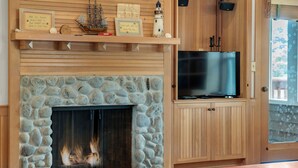 Ein Kamin aus Stein mit einem Fernseher auf einem Holzboden, ein Regal mit Dekoration und Blick ins Freie.