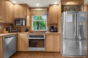 A modern kitchen with wooden cabinets, stainless steel appliances, and a window with a view of trees. - Beachcomber's Retreat *Beach*Golf*Pets (Gearhart)