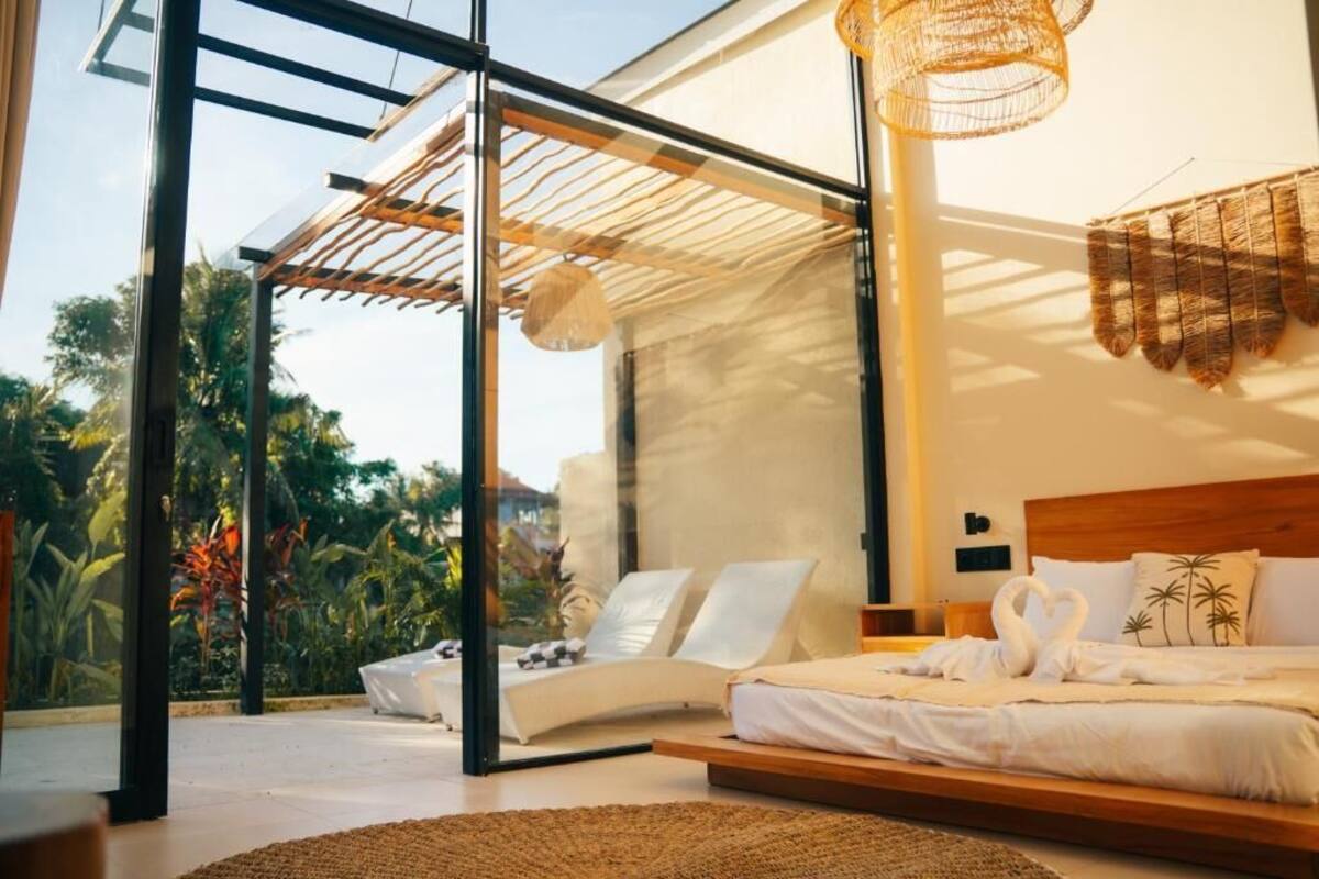 A modern bedroom with a glass door leading to a balcony, a bed with white linens, and a woven light fixture.