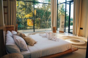 Un dormitorio con un ventanal grande, una cama con almohadas, una mesita de noche y una alfombra decorativa.