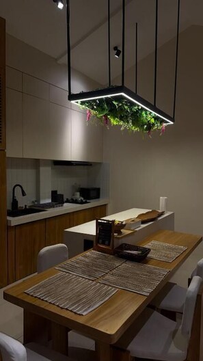 Une cuisine moderne avec une table à manger en bois, des chaises blanches et un luminaire suspendu agrémenté de plantes.