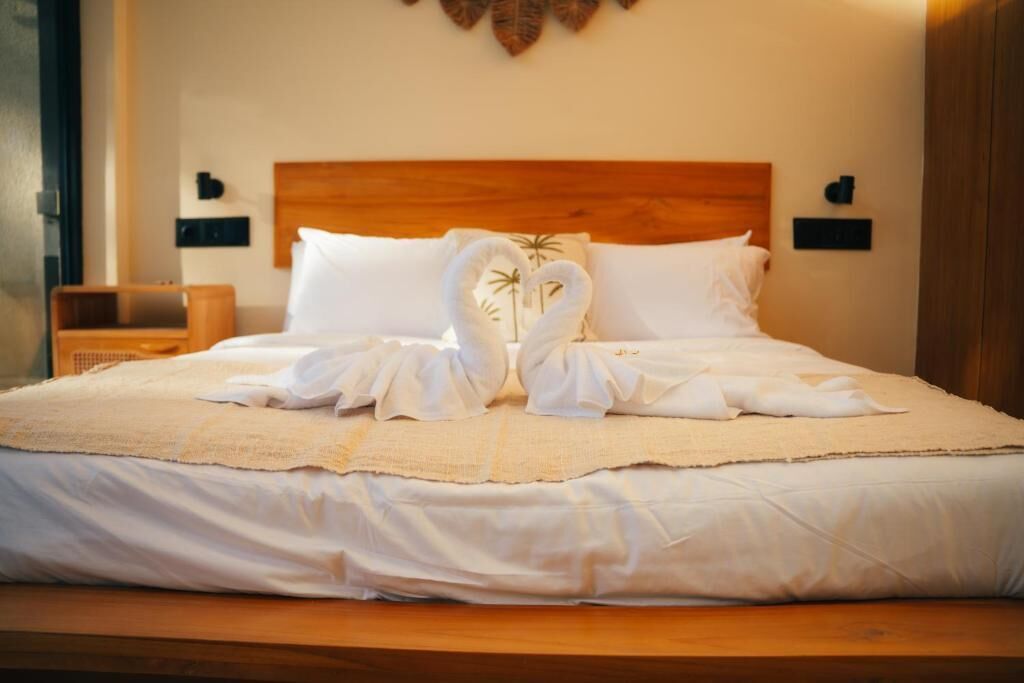 A neatly made bed with a wooden headboard, white linens, and two towels arranged in a heart shape.