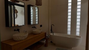 Un baño con una bañera independiente, dos lavamanos con lavabos de piedra y espejos sobre ellos.