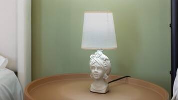 A white table lamp with a white lampshade on a round table against a green wall.