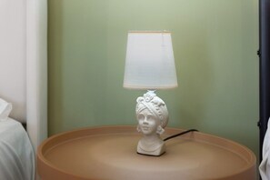 A white table lamp with a white lampshade on a round table against a green wall.