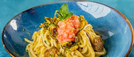 A plate of pasta with vegetables and a garnish on a blue plate.