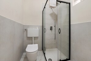 A modern bathroom with a toilet, a glass-enclosed shower, and a white sink.