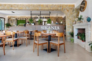 L’intérieur d’un restaurant présente des murs en pierre, des tables et des chaises en bois, un coin bar et une cheminée.