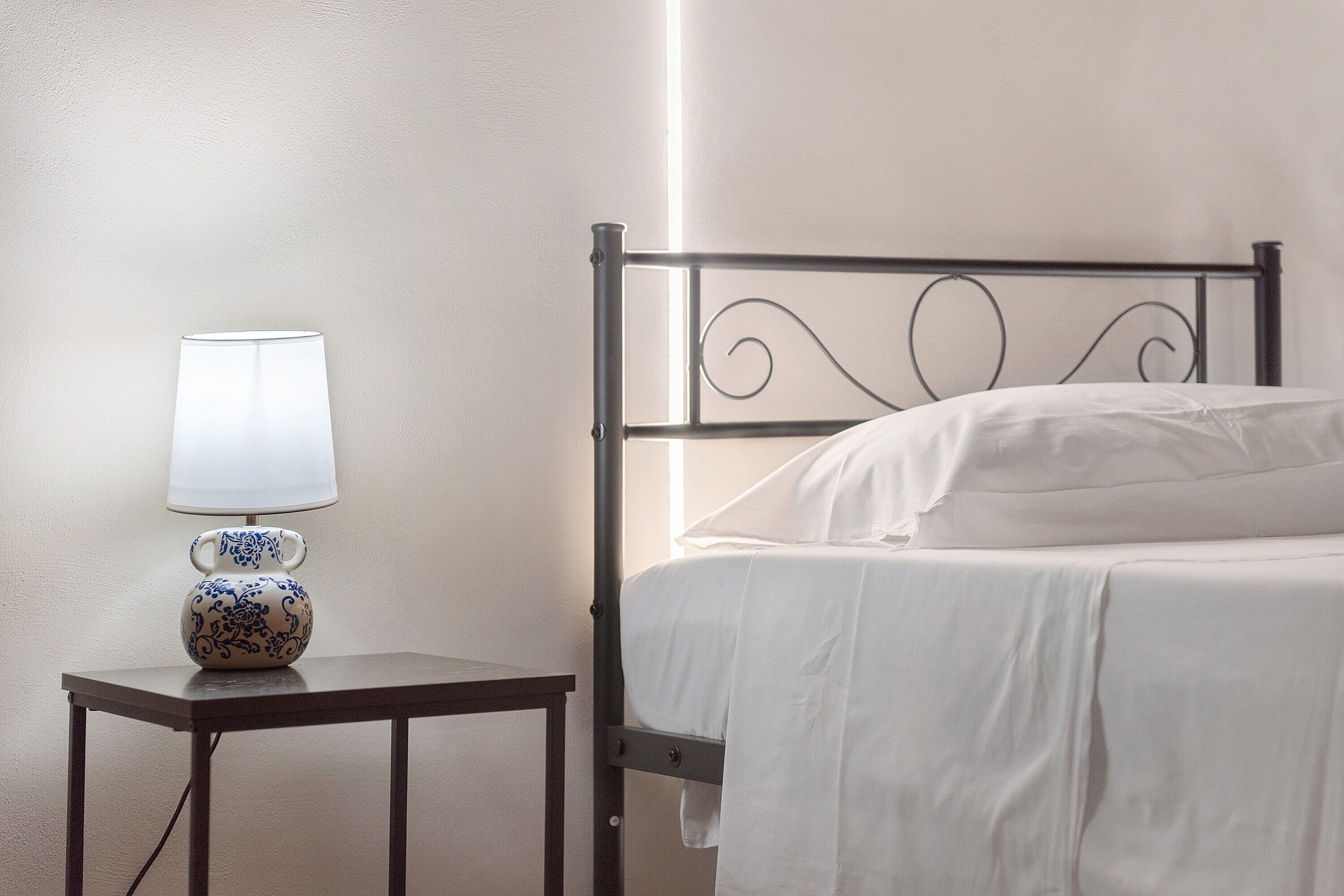 Ein Einzelbett mit weißer Matratze und Kissen, ein Nachttisch mit Lampe sowie eine Wand mit strukturierter Oberfläche.