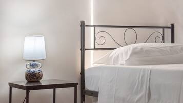 Ein Einzelbett mit weißer Matratze und Kissen, ein Nachttisch mit Lampe sowie eine Wand mit strukturierter Oberfläche.