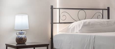 A single bed with a white mattress and pillows, a bedside table with a lamp, and a wall with a textured finish.