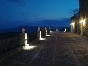 Un camino empedrado que lleva a un edificio de fachada de piedra con vistas a las montañas al fondo.