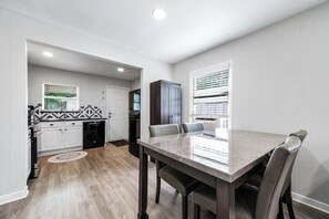 Una cocina moderna con armarios blancos, un mueble de madera oscura y un comedor con mesa de mármol y sillas de cuero.