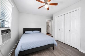 A bedroom with a bed, a ceiling fan, white walls, a wooden floor, and a white door. - House with Security Gate - 7 min from downtown Houston (Houston)