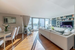 Ein modernes Wohnzimmer mit Essbereich, großen Fenstern und einem Fernseher.
